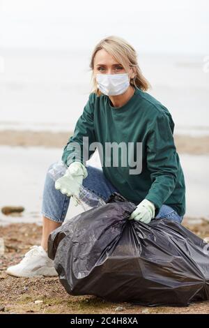 Portrait der jungen Frau in Schutzmaske Blick auf Kamera, während das Setzen von Plastikflaschen in Tasche im Freien Stockfoto