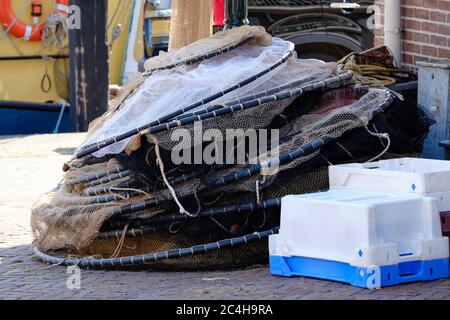 Fischernetze in Bündeln gelagert, im Freien auf dem Boden gestapelt, weiße und blaue Boxen vor, Schiff im Hintergrund Stockfoto