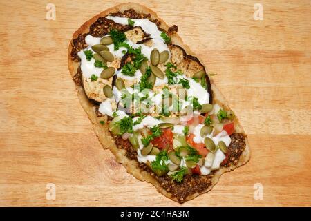 HAUSGEMACHTES MITTELÖSTLICHES FLADENBROT MIT GEGRILLTER AUBERGINE, ZATAR, GURKE, TOMATENZWIEBEL, KÜRBISKERNEN, PETERSILIE UND JOGHURT Stockfoto