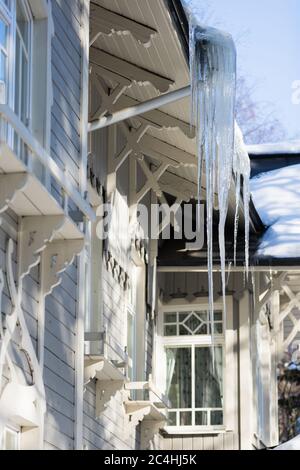 Eis Stalaktit hängen vom Dach mit Holzwand. Gebäude mit großen Eiszapfen bedeckt. Eiszapfen sind sehr gefährlich für das Leben. Schlechte thermische Isolierung Stockfoto