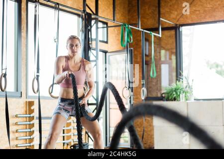 Junge Frau im Fitnessstudio Trainingscrossfit an den Seilen Stockfoto