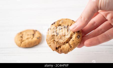 Schokoladenkeksen in der Hand. Hand halten Cookie mit Schokolade Tropfen auf weißem Holzhintergrund. Amerikanischer Keks Stockfoto