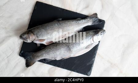 Zwei Regenbogenforellen auf einem schwarzen Steinbrett. Fisch für Suppe vorbereitet. Fisch Suppe Zutat. Ausschneiden der Fische Stockfoto