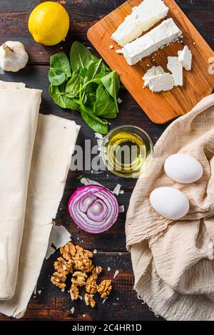 Griechische spanakopita Zutaten Filo Spinat Eier Feta Draufsicht auf dunklen Holzhintergrund. Stockfoto