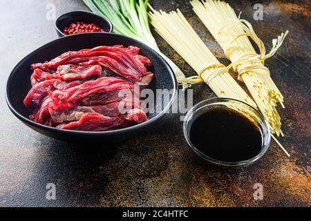 Rohzutaten für Rührei Chinesische Nudeln mit Gemüse und Rindfleisch in schwarzer Schüssel braten. Auf alten rustikalen Tisch. Seitenansicht Stockfoto