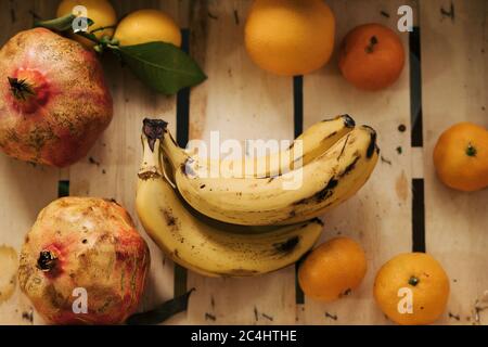 Ein Bündel Bananen in einer Holzkiste, umgeben von Mandarine, Zitronen, Orange und Granatäpfeln. Stockfoto