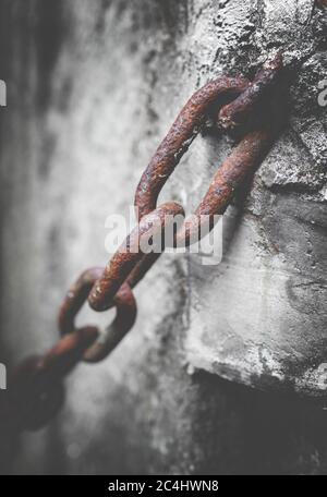 Rostige Kette im Zement. Rostige Kette, die am Zementmast verankert ist. Unscharfe Hintergrundunschärfe. Foto im Retro-Stil. Stockfoto