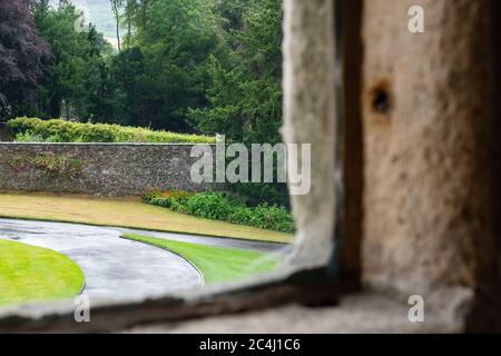 Von unten aus hat man einen Blick auf ein Fenster in einem alten Gebäude. Steinarbeiten Konstruktion ist im Vordergrund und entfernten Bäumen vor dem Fenster zu sehen. Stockfoto