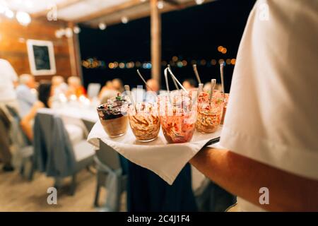Der Kellner nimmt das leere schmutzige Geschirr vom Nachtisch. Eine Nahaufnahme des Geschirrs auf dem Tablett in den Händen eines Mannes. Stockfoto
