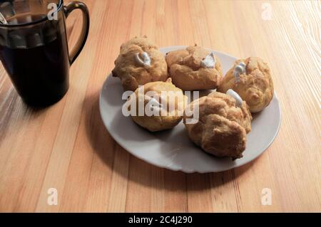Eine Portion Eclare gefüllt mit Schlagsahne mit einer Tasse Tee auf einem Holzhintergrund. Stapeln Sie Pudding Cookies und Tee. Eclairs auf einer weißen Platte und ein t Stockfoto