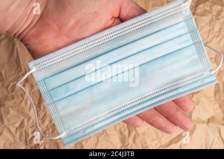 Medizinische schützende chirurgische Maske in der Hand auf einem Hintergrund von zerknittert Verpackung braunes Papier. Nahaufnahme Stockfoto