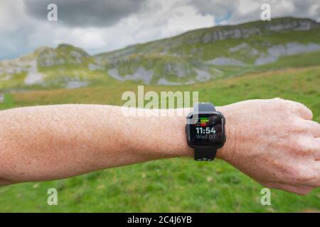 Erwachsener Mann, der einen beliebten Fitness-Tracker am linken Handgelenk trägt. Der Mann ist ein Trailrunner und schaut in angezeigte Statistiken. Stockfoto