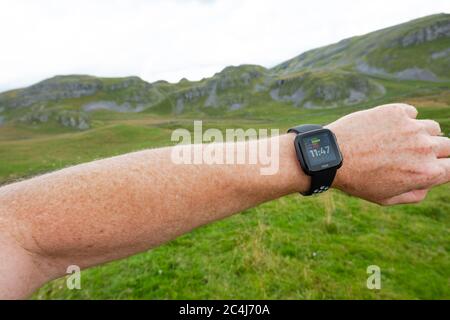 Erwachsener Mann, der einen beliebten Fitness-Tracker am linken Handgelenk trägt. Der Mann ist ein Trailrunner und schaut in angezeigte Statistiken. Stockfoto