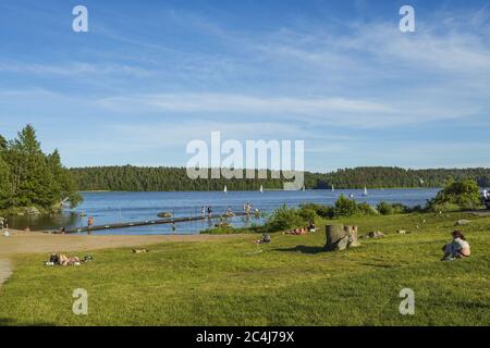 Wunderschöne Aussicht auf die Seenlandschaft. Leute auf Plattform versuchen Wasser. Weiße Segelboote am Horizont. Schweden. Europa. Uppsala. Stockfoto