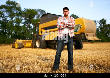 Portrait des stolzen Harvester-Maschinentreibers mit gekreuzten Händen auf der Brust. Bauer steht an seinem Mähdrescher. Agronom schaut auf die Kamera. Rancher bei Stockfoto