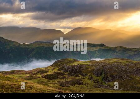 Wunderschöne goldene Sonnenstrahlen an EINEM Misty-Morgen im englischen Lake District durch Wolken brechen. Stockfoto