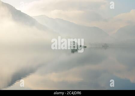 Isolierte Insel spiegelt sich in EINEM ruhigen ruhigen See an EINEM friedlichen Misty Sommermorgen. Lake District, Großbritannien. Stockfoto