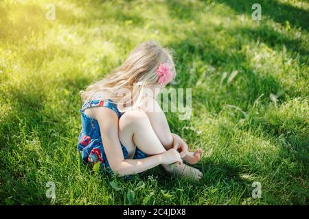 Traurige junge Mädchen auf dem Boden sitzen im Freien am Sommer sonnigen Tag. Nachdenkliche kleine Kind träumen Denken. Unsicher einsamen Kind versucht, mit Stress p zu bewältigen Stockfoto