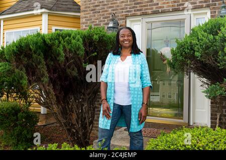 Lächelnde afroamerikanische Frau, die vor ihrem Haus steht Stockfoto