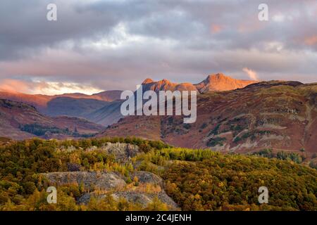 Die Langdale Pikes Mountain Range Bei Sonnenaufgang, Wenn Morgenlicht Aus Dunklen Moody Clouds Erleuchtet. Lake District, Großbritannien. Stockfoto