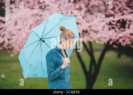 Porträt einer Frau mit blauem Regenschirm vor Die Frühlingsblüte Stockfoto