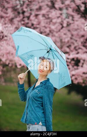 Porträt einer Frau mit blauem Regenschirm vor Die Frühlingsblüte Stockfoto
