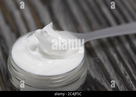 Plastikflasche mit Sahne. Neben dem Schulterblatt, darauf eine Creme. Vor dem Hintergrund von Kiefernholzplatten. Stockfoto