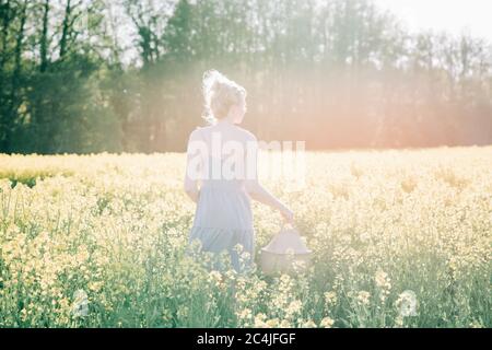 Frau stand in einem gelben Blumenfeld und hielt einen Korb Bei Sonnenuntergang Stockfoto