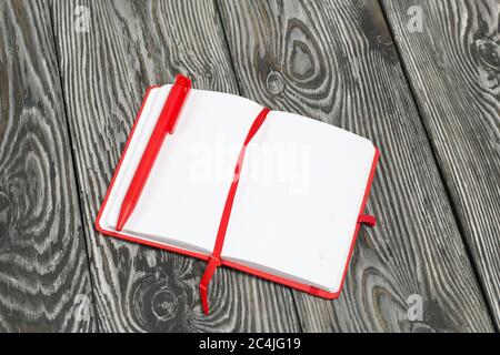 Rotes Notizbuch und Stift geöffnet. Vor dem Hintergrund von Kiefernholzplatten, in schwarz und weiß lackiert. Stockfoto
