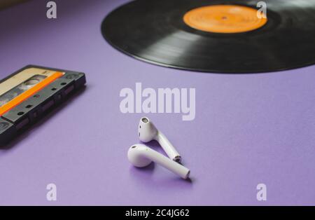 Draufsicht auf eine lange Vinyl-Schallplatte, schwarzer Kopfhörer und eine Audiokassette auf dem violetten Hintergrund. Konzept der Entwicklung der Musik. Stockfoto