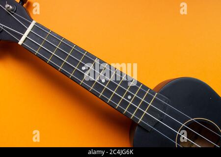 Korpus einer grell schwarzen Ukulele Gitarre vor einem grell orangenen Hintergrund (Minimalismus-Stil), Kopierraum für Text Stockfoto