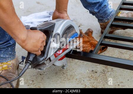 Arbeiter mit einer Kreissäge zu schneiden ein quadratisches Metallgeländer Schneider verwenden Schneidwerkzeuge Stockfoto