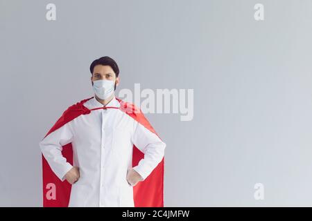 Selbstbewusster Arzt im Superhelden Kostüm und Schutzmaske auf grauem Hintergrund, Leerraum Stockfoto