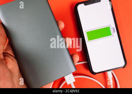 Smartphone auf rotem Hintergrund mit einem Symbol für niedrigen Akkustand auf dem Bildschirm. Stockfoto