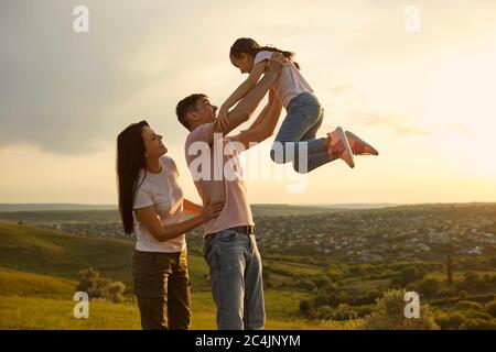 Fröhliche junge Familie, die Spaß mit ihrer Tochter in den Bergen bei Sonnenuntergang. Vater hob sein Kind auf dem Land Stockfoto