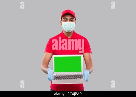 Lieferung Mann zeigt Laptop Green Screen Tragen medizinische Maske und Handschuhe. Home-Bestellungen, Quarantäne-Lieferung, Online-Shopping, Freiberufler-Konzept. Stockfoto