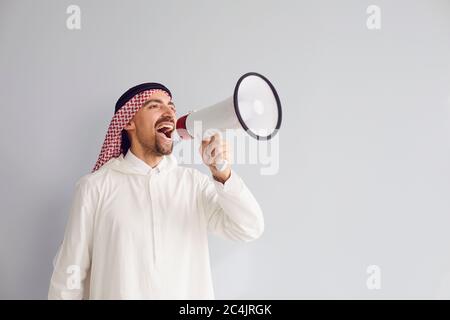 Arabischer Mann mit einem Megaphon in der Hand schreiende Anrufe wirbt Angebote auf grauem Hintergrund für Text. Stockfoto