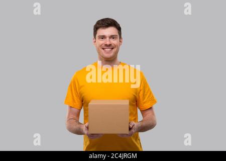 Delivery man mit Box in den Händen. Gelbe T-Shirt Lieferung Junge. Lieferung Nach Hause. Quarantäne-Held. Mann Lächelt Stockfoto