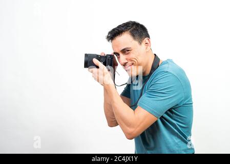 Lächelnder Mann mit einer Fotokamera in den Händen und Blick auf die Kamera. Seitenansicht. Mittlerer Schuss. Weißer Hintergrund. Stockfoto