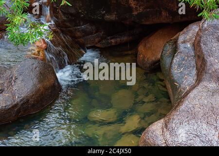 Ein Felsenpool in den Bergen mit einem kleinen Wasserfall, der das Wasser wirbelt Stockfoto