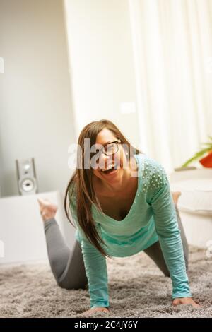 Lachen einer jungen Frau auf ihrem Teppich in ihrem Haus mit den Händen auf dem Teppich, Brille tragend Stockfoto