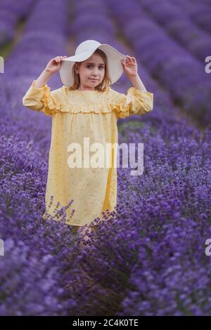 Lächelndes kleines Mädchen in gelbem Kleid und weißem Hut bleiben in einem Lavendelfeld Stockfoto