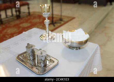 Katholische liturgische Gegenstände bereit auf dem Tisch in der Kirche. Kelch, Kommunion Waffeln, Wein und Wasserkrüge Stockfoto