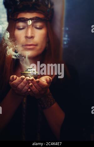 Weihrauch in einer Frauenhand, Weihrauchrauch auf einem unscharfen Hintergrund. Stockfoto