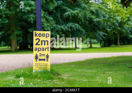 Halten Sie sich 2 Meter auseinander Schild nach links in einem Park Stockfoto