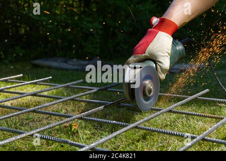 Schneiden Metallnetz mit Mühle auf grünem Gras. Funken von Kontaktmaterialien. Arbeiter draußen, schneiden Sie das Stahlnetz. Prozess mit Winkelschleifer. Stockfoto