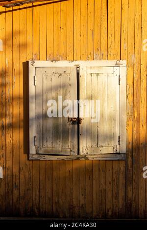 Weiße Fensterläden auf einem gelben Haus. Geschlossenes Fenster. Stockfoto