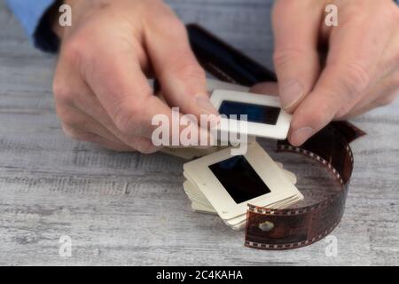 Ein älterer Mann sieht sich einen Stapel von 35 mm Dias alter Fotografien in seinen rauen Händen an Stockfoto