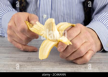 Nahaufnahme der Hände eines älteren Mannes, der eine reife Banane schält Stockfoto