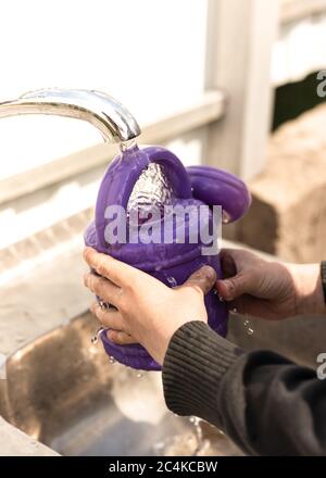 Der Junge gießt Wasser aus einem Wasserhahn in eine violette Gießkanne Stockfoto